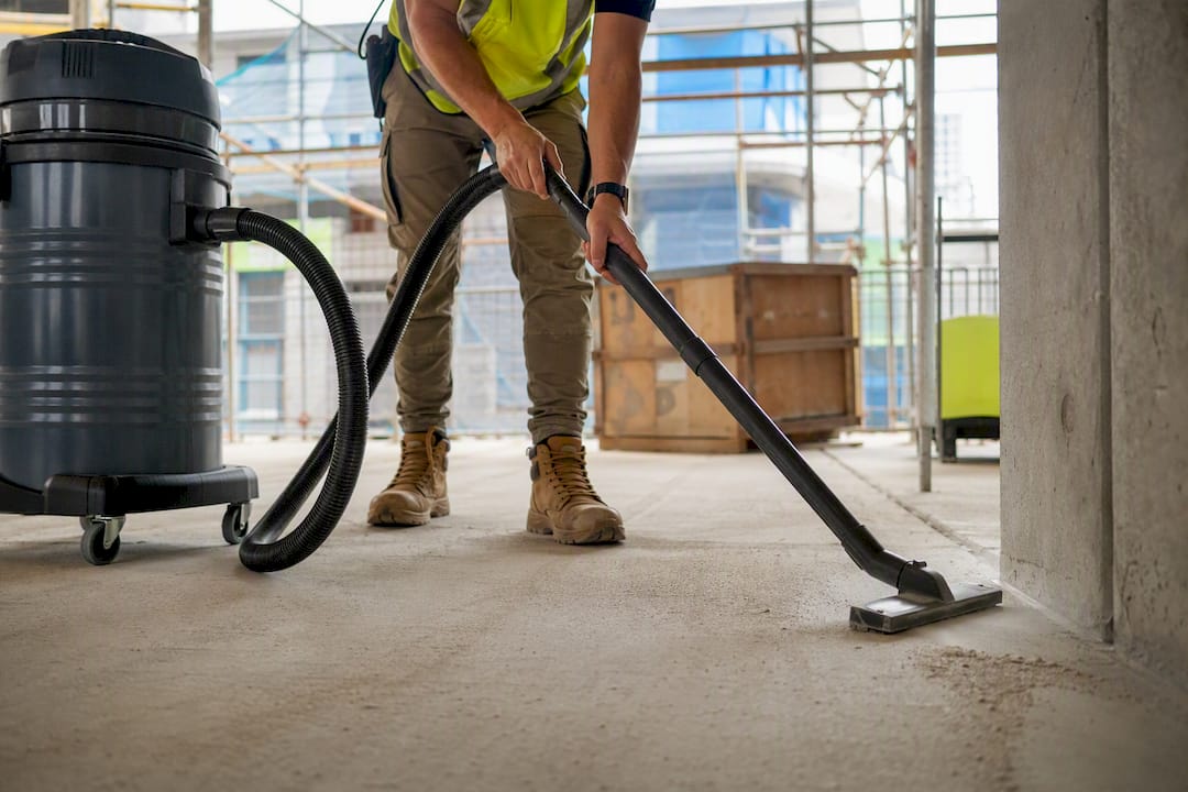 Worker using HEPA vacuum cleaner on concrete floor