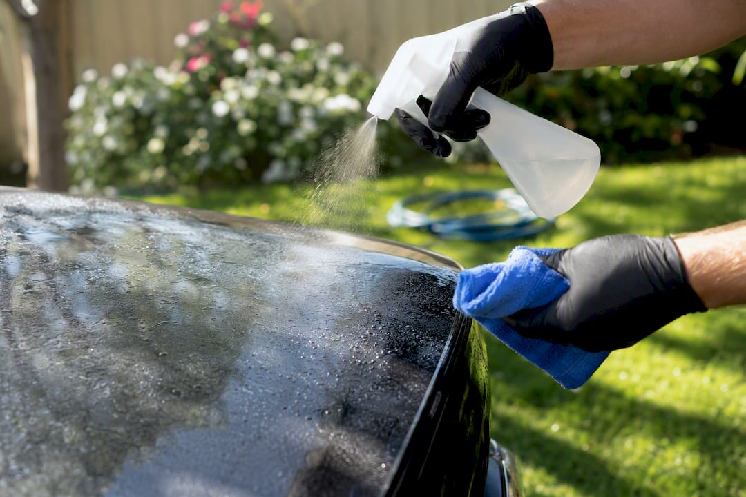 Gloved hand soaking bird droppings on car bonnet